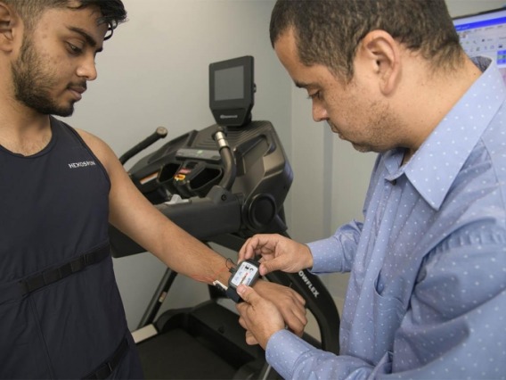 Man placing research device on patient's wrist, treadmill in background